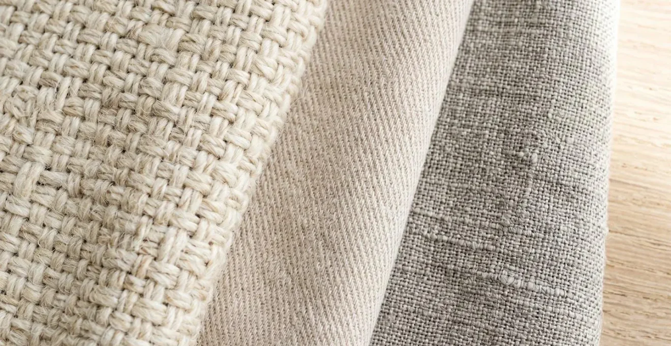 Gros plan sur des rouleaux de tissus nobles superposés montrant les textures contrastées de la laine, du coton et du lin